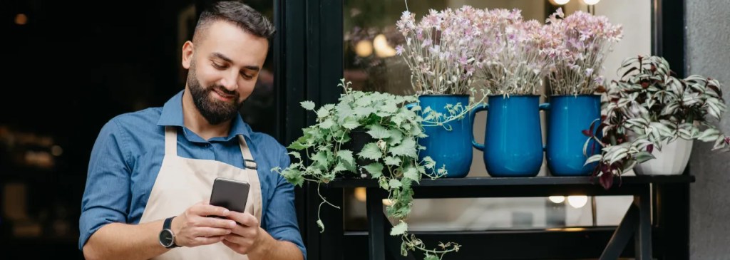 Un fleuriste devant sa boutique en train de répondre à un message sur WhatsApp