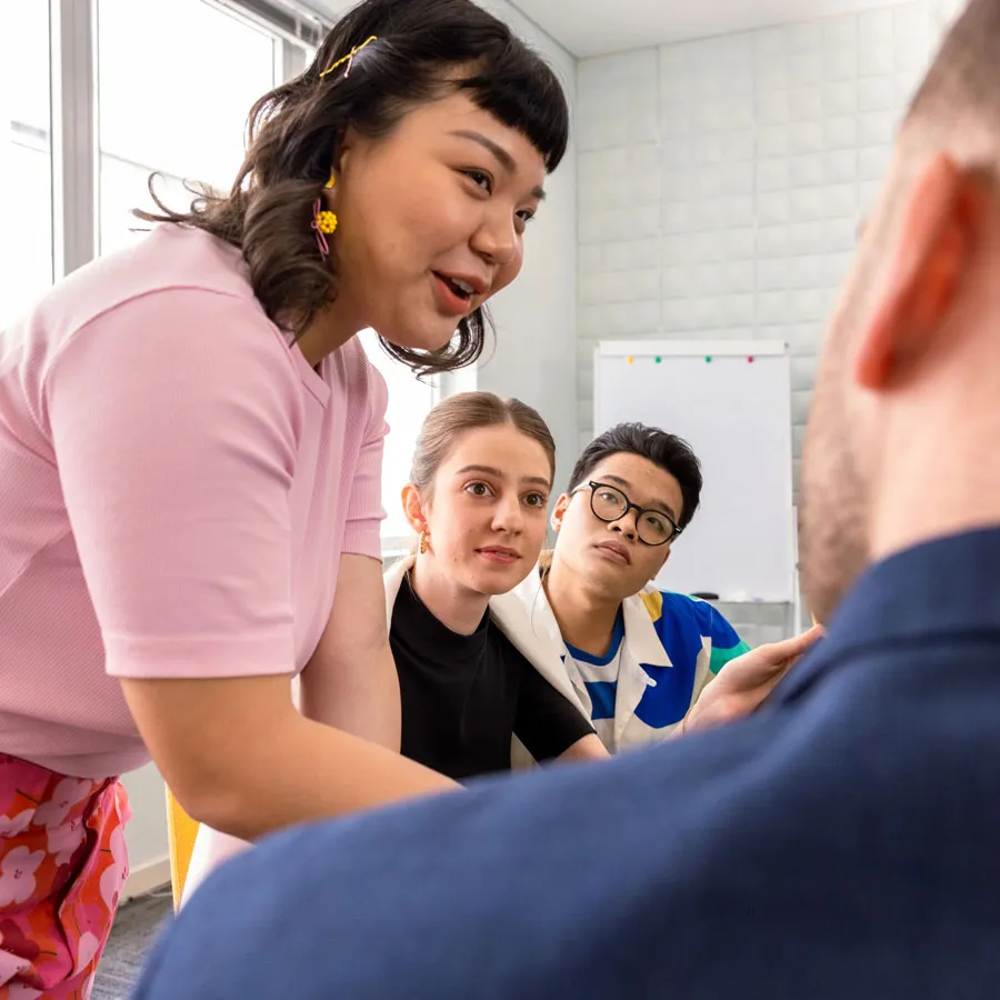 Office meeting where a woman is speaking to a man while two other people are observing the conversation