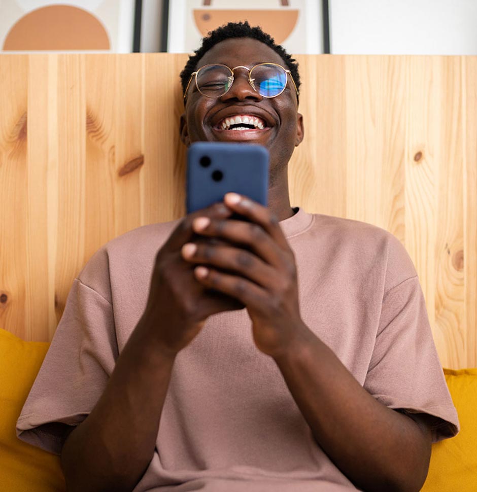A man sitting down, holding his phone and laughing