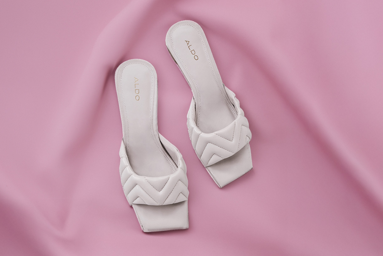 A pair of white dress shoes against a pink backdrop.