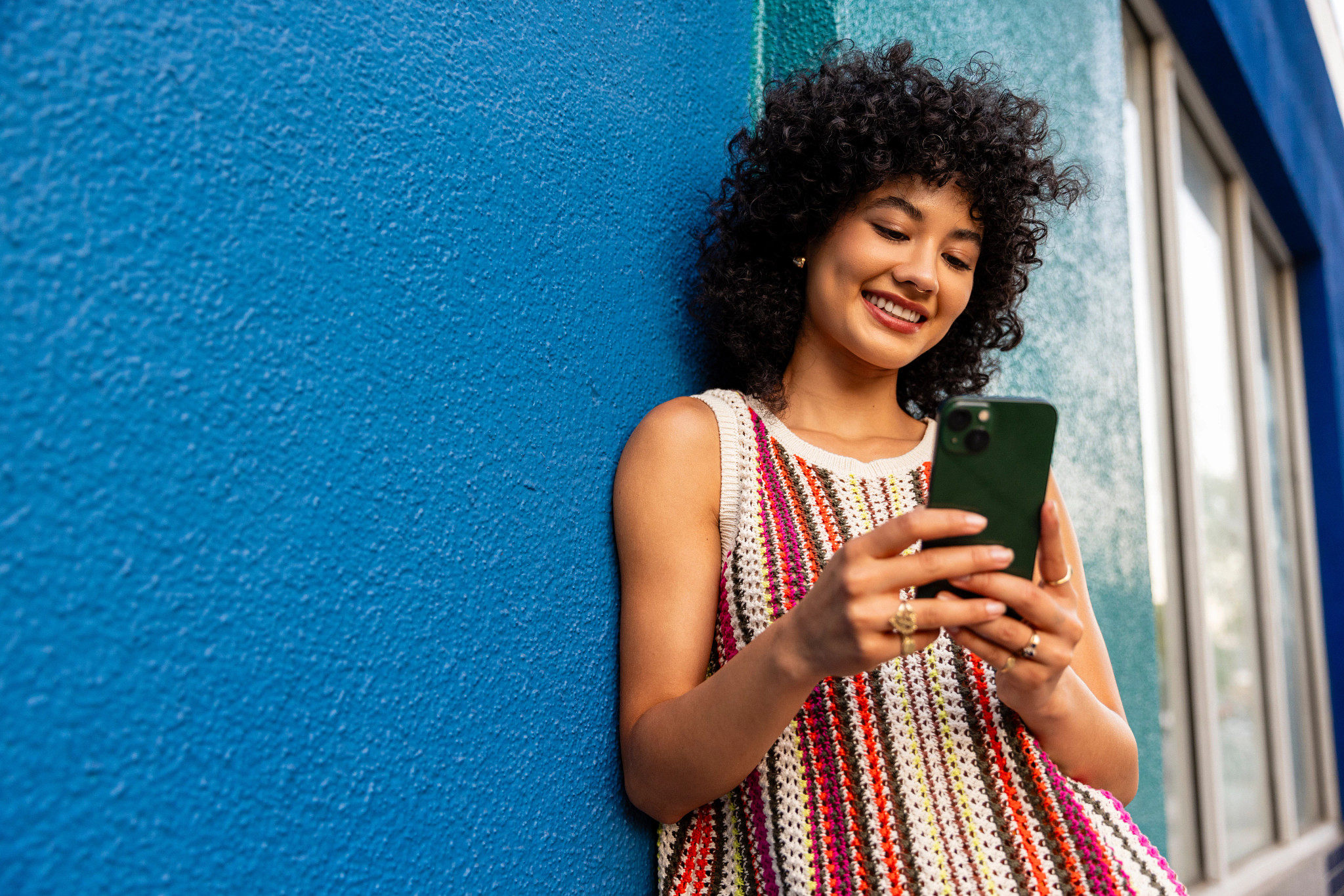 A woman uses her mobile phone while leaning against a wall.
