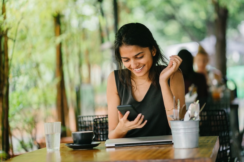 A woman sitting at a table laughing while looking at her phone