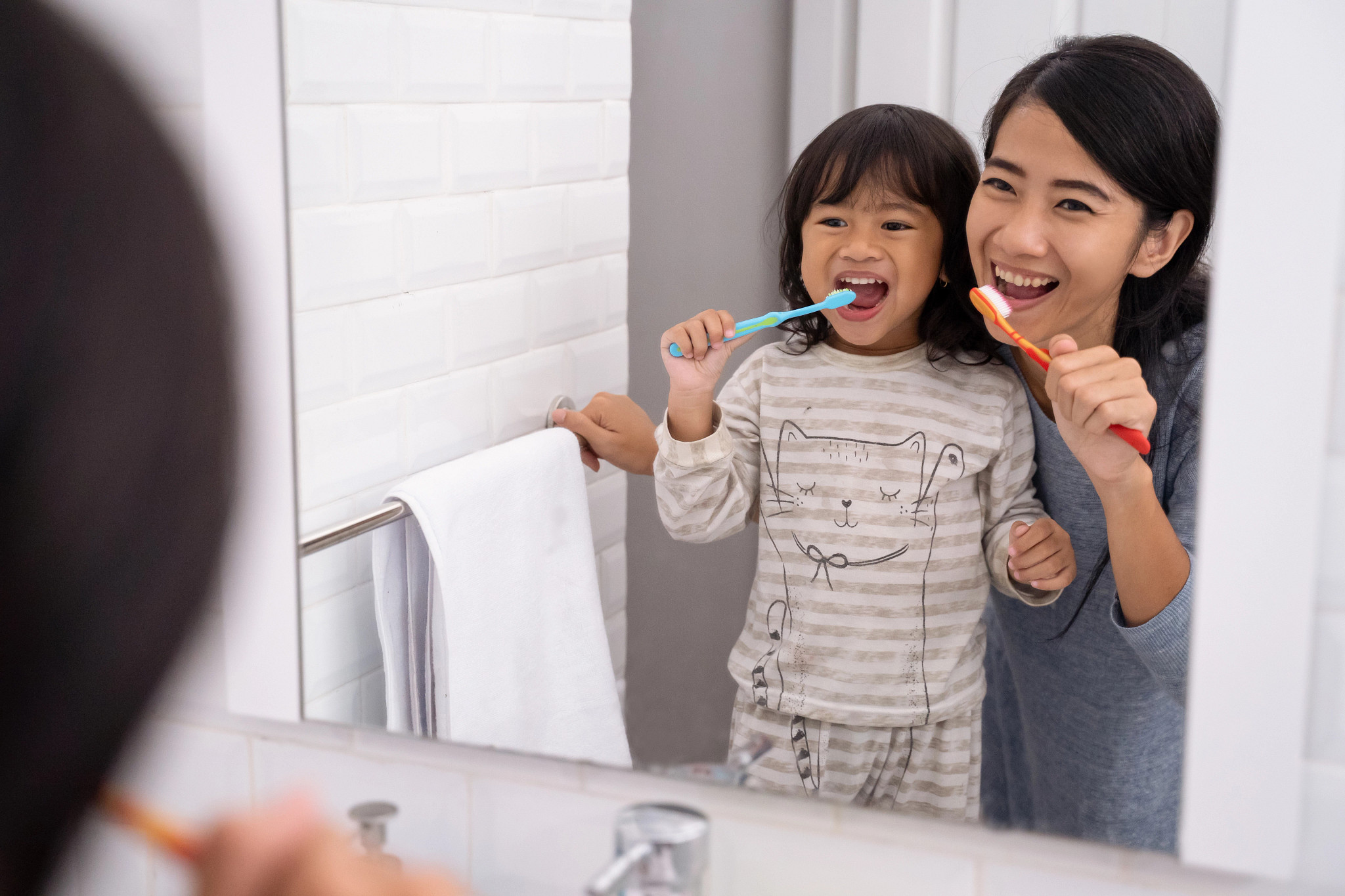A mother and daughter brushing their teeth together.