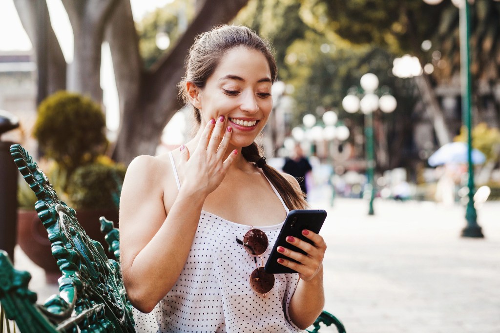 Une femme en train de regarder son téléphone et de sourire.