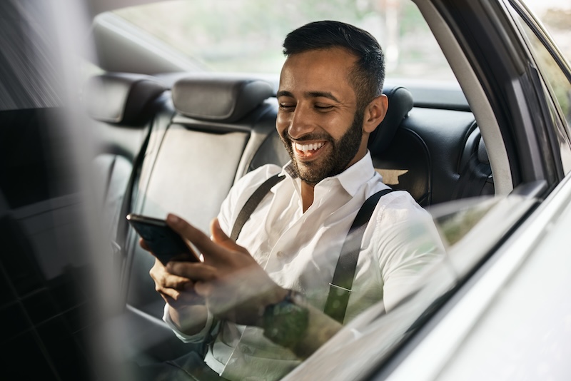 A man in the back seat of a car laughing while looking at his phone