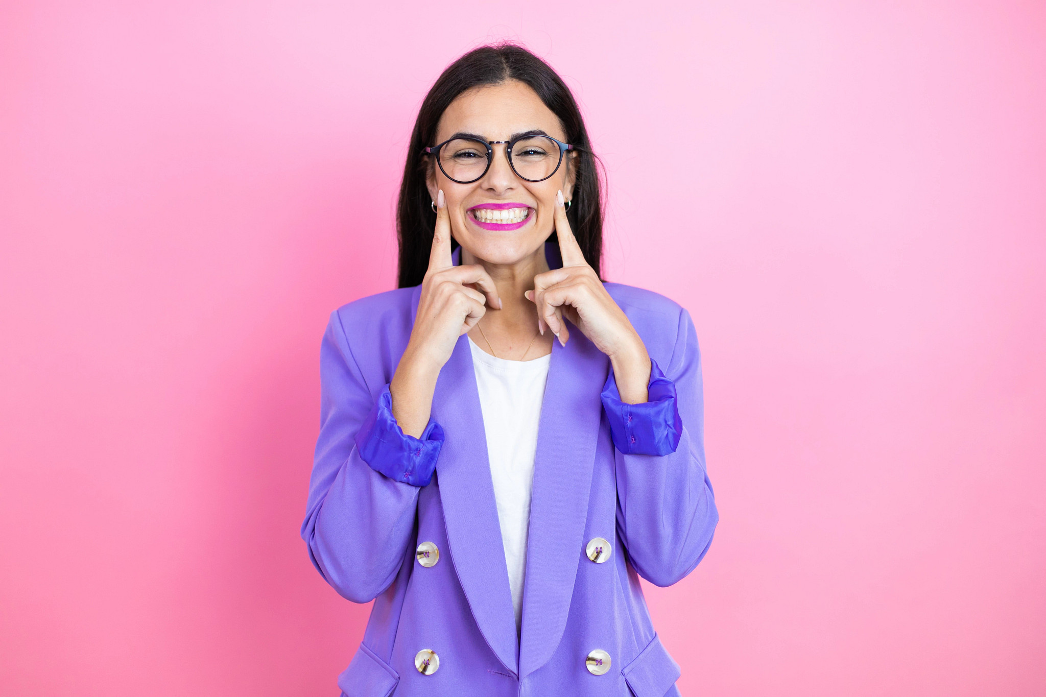 woman standing in front of pink background smiling in purple blazer