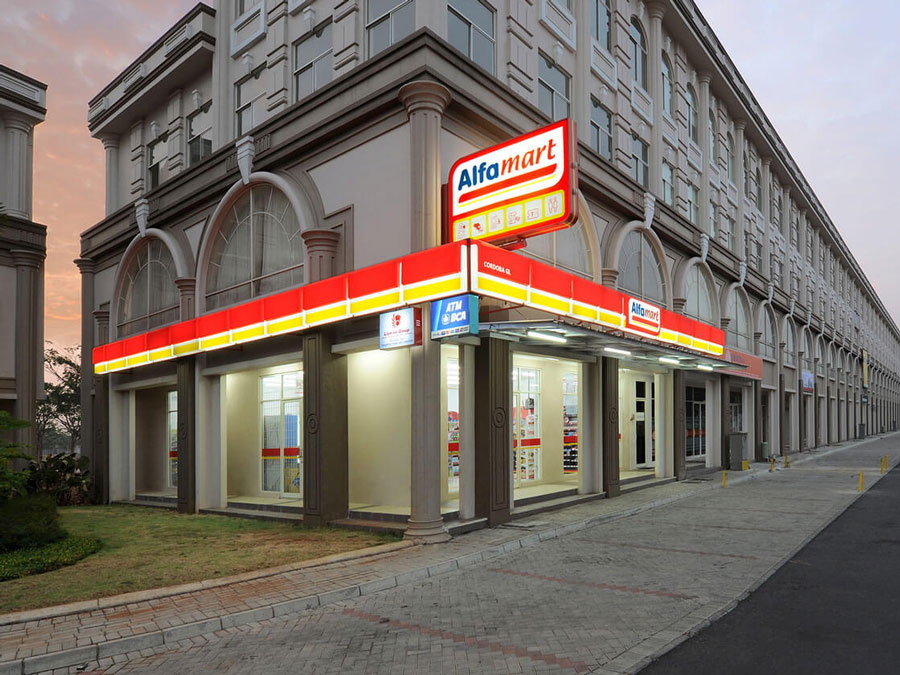 Entrada de una tienda de comestibles de Alfamart con letreros y puerta de cristal.