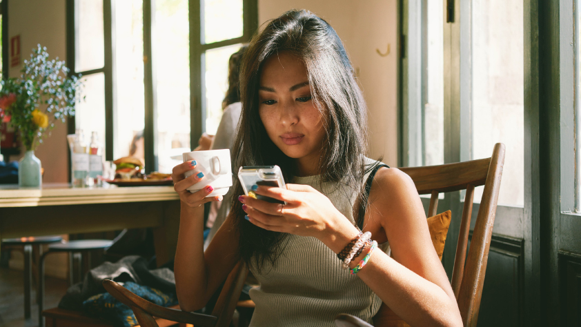 Persona sentada en una cafetería bebiendo café mientras lee un mensaje de WhatsApp