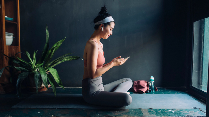 Persona sentada sobre una esterilla de yoga mirando el teléfono después de la clase