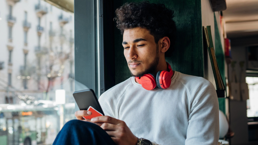 A person sitting in a cafe with headphones around their neck while reading a financial services message through WhatsApp on phone
