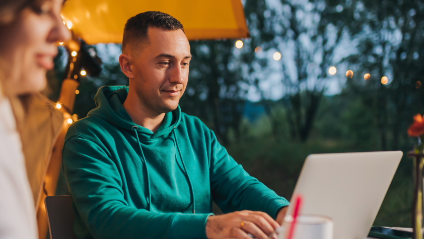 Personne assise sur une terrasse le soir. Elle porte un sweat-shirt vert et travaille sur un ordinateur portable.