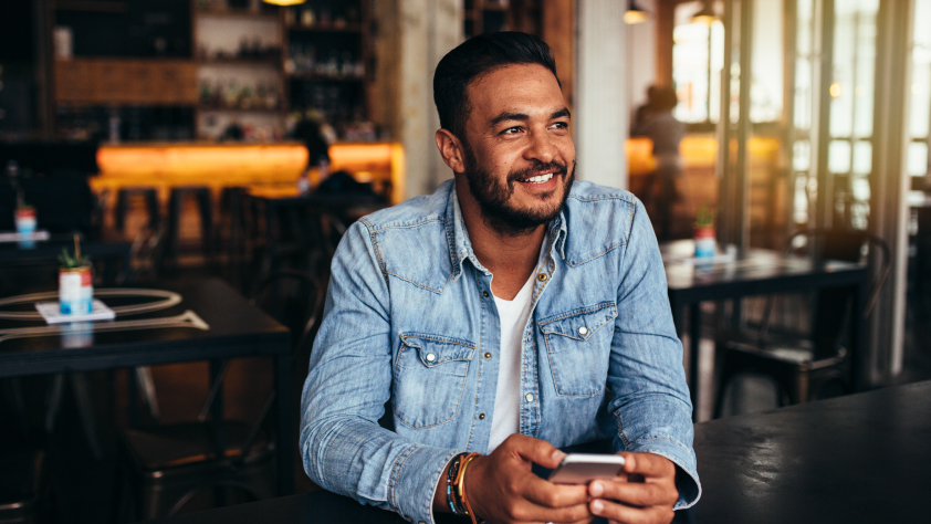 Personne assise dans un restaurant, portant une chemise en jean et tenant un téléphone tout en regardant par la fenêtre.