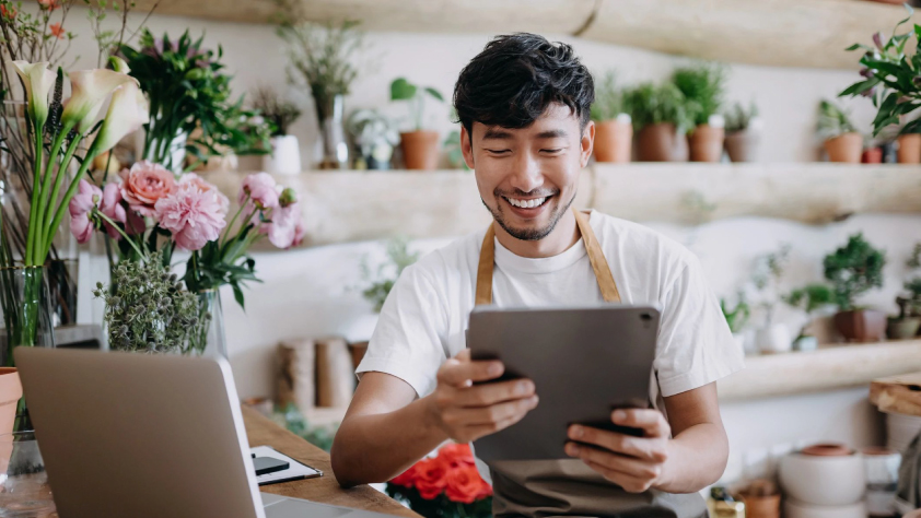 Plant shop owner smiling at online orders showing on iPad