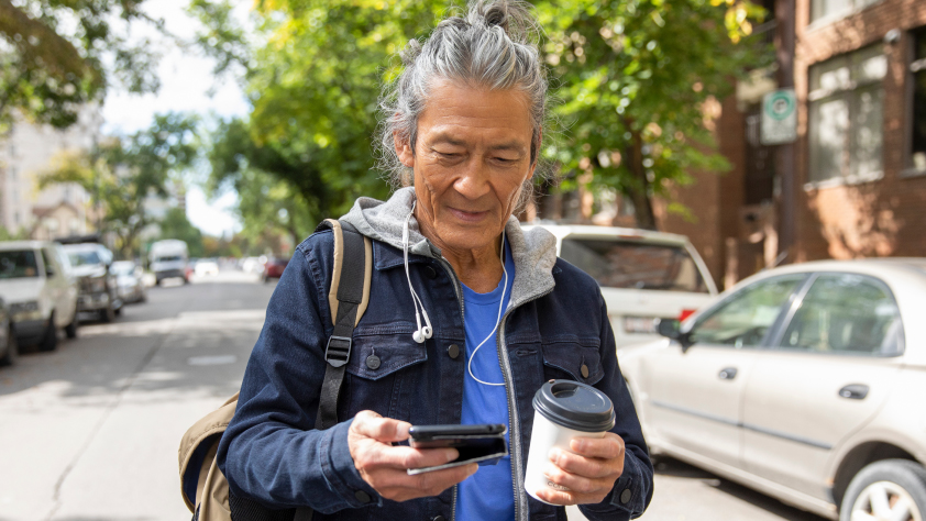 Persona caminando por la calle leyendo un mensaje de WhatsApp en el teléfono y sosteniendo un café