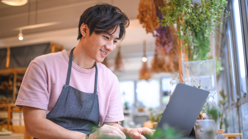 Small business owner in plant shop messaging a new customer on laptop via WhatsApp