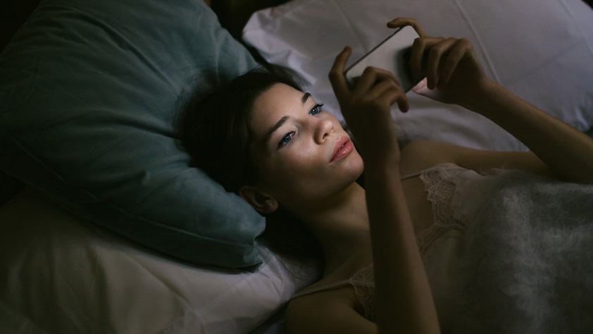 Seseorang berbaring di tempat tidur sambil melakukan percakapan bisnis di WhatsApp untuk melakukan pembelian