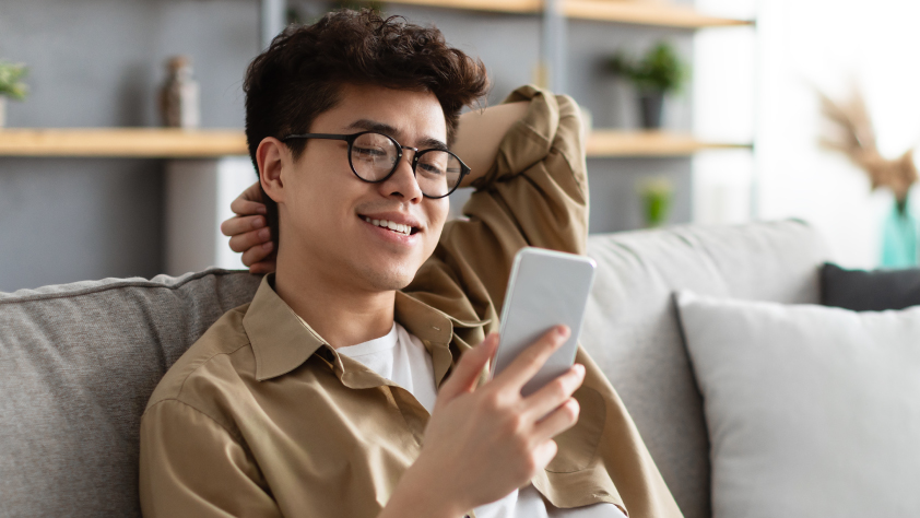 Personne souriante portant des lunettes, assise sur un canapé dans un bureau et lisant un message WhatsApp d’Akulaku