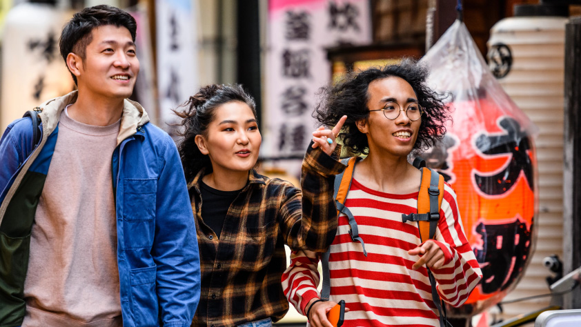 Tiga orang berjalan di depan etalase toko Asia