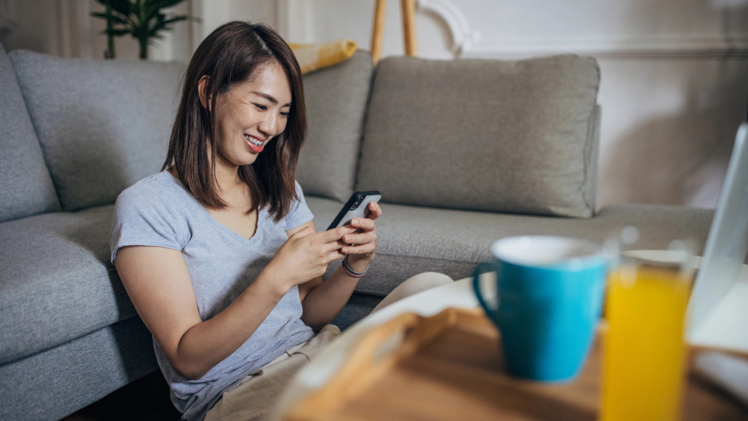 Personne souriante assise par terre contre un canapé, passant commande de jean sur WhatsApp