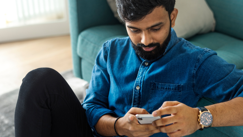 Personne assise par terre, dos à un canapé bleu, pendant une conversation WhatsApp au téléphone