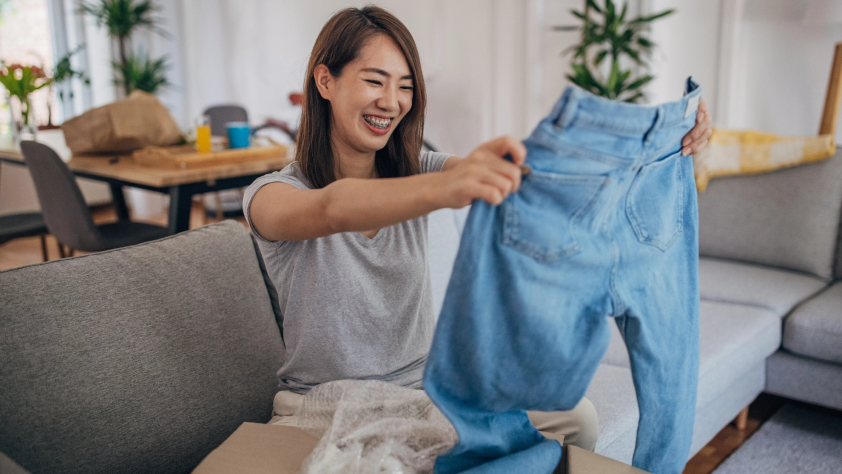 Personne assise sur un canapé ouvrant un paquet avec un nouveau jean