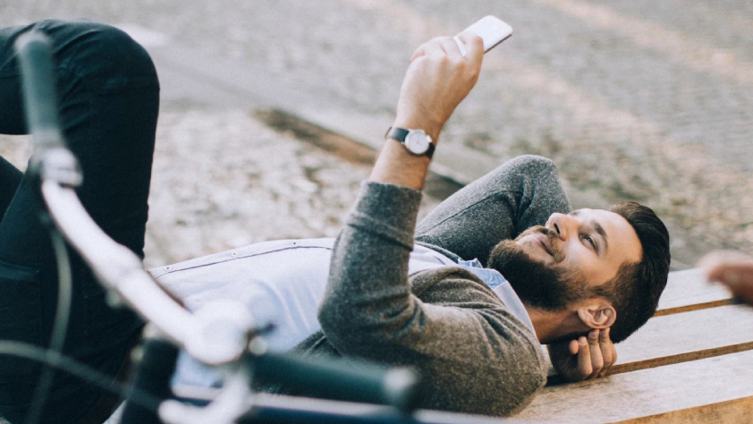 Une personne sourit, allongée sur un banc en extérieur, et lit un message marketing sur son téléphone via WhatsApp