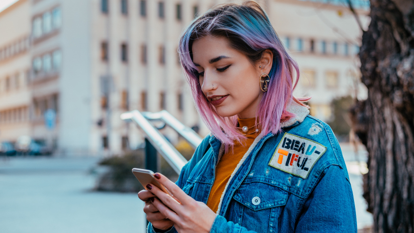 Une personne debout dans la rue portant une veste en jean et lisant un message promotionnel sur WhatsApp sur son téléphone