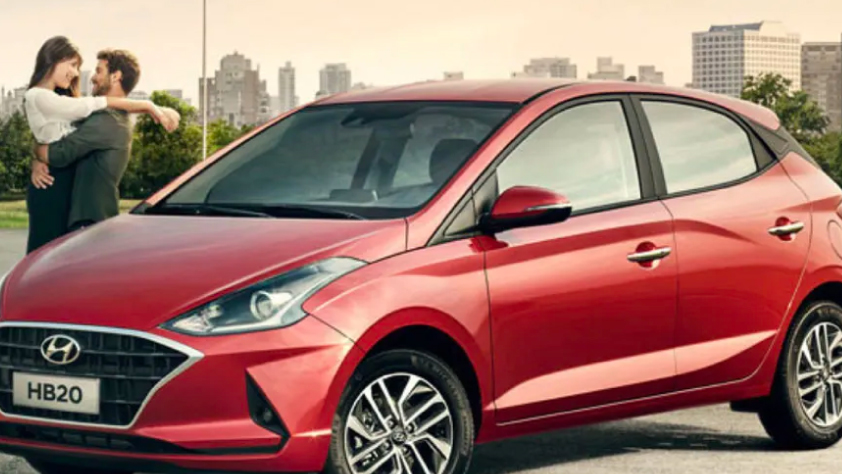 Un couple s’embrasse à côté d’une Hyundai rouge, avec la silhouette de la ville en arrière-plan.