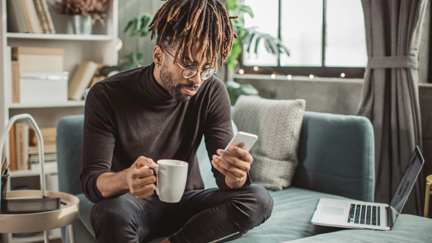 Personne assise sur un canapé en train de boire un café tout en lisant un message WhatsApp