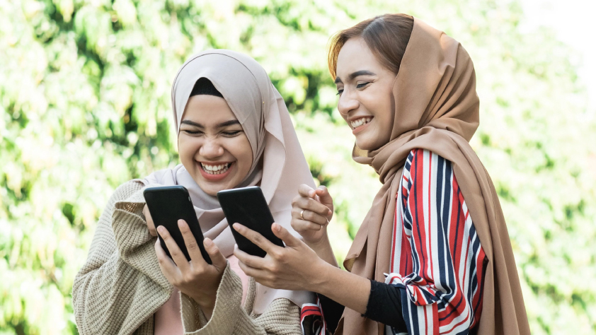 Dua orang tertawa sambil menunjukkan iklan di telepon mereka