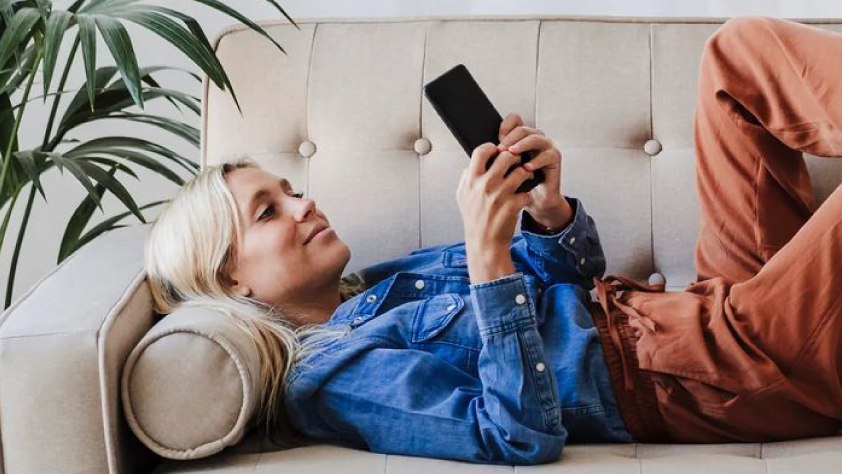 Seseorang berbaring di sofa sambil melihat iklan Facebook di ponsel
