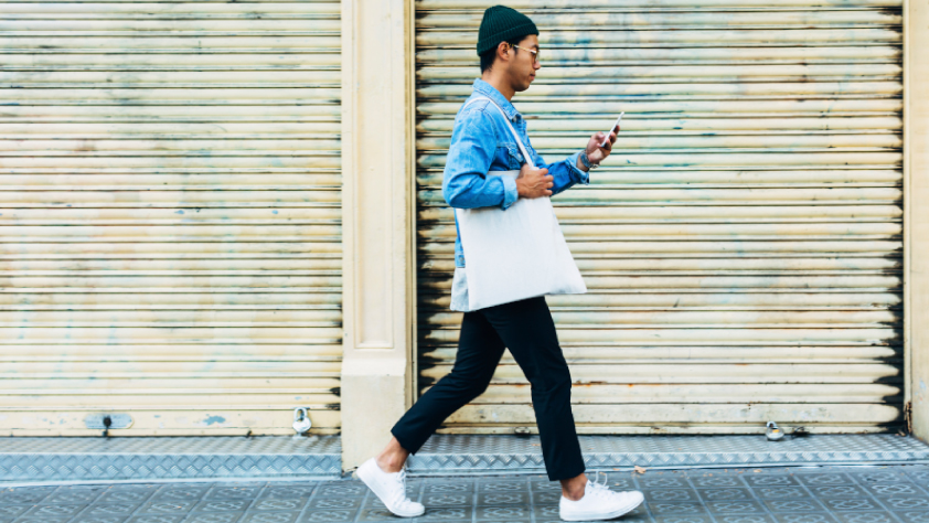 Une personne qui marche dans la rue en envoyant un message WhatsApp à une entreprise pour effectuer un achat