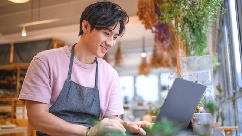 Pemilik bisnis kecil bekerja menggunakan laptop di toko tanamannya