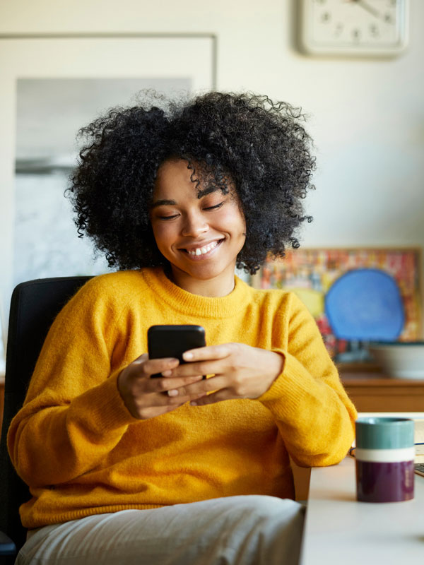 A woman smiling and looking at her phone while sitting at her desk