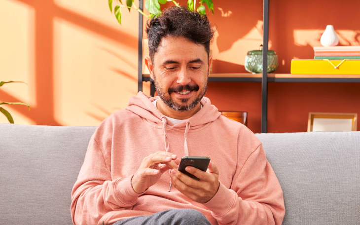Person sitting on couch smiling at and scrolling on phone