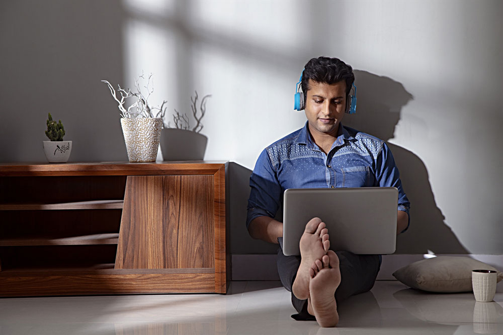 A man seated on the floor, engrossed in reading on his laptop.