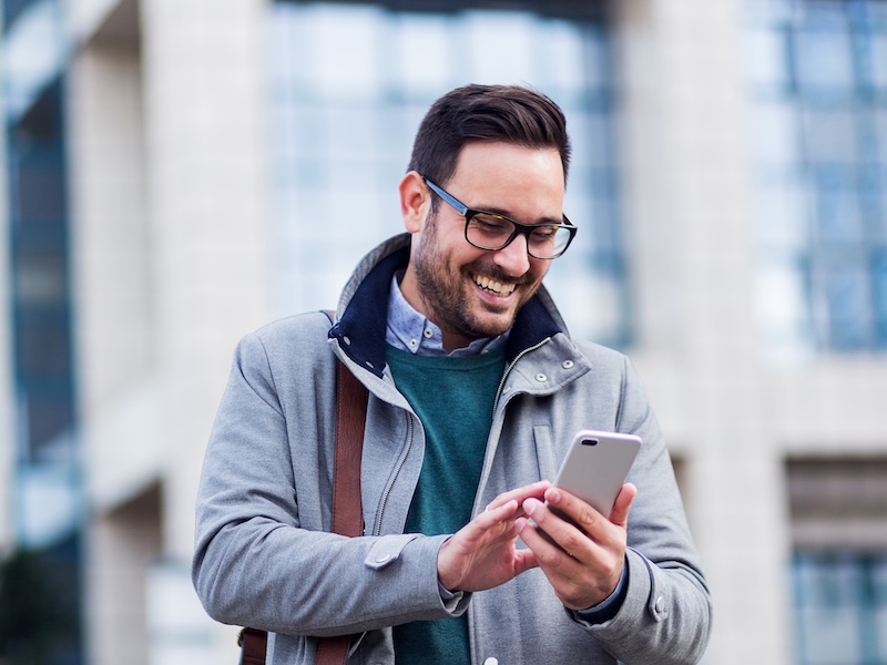 Man in gray coat smiling while looking down at his phone