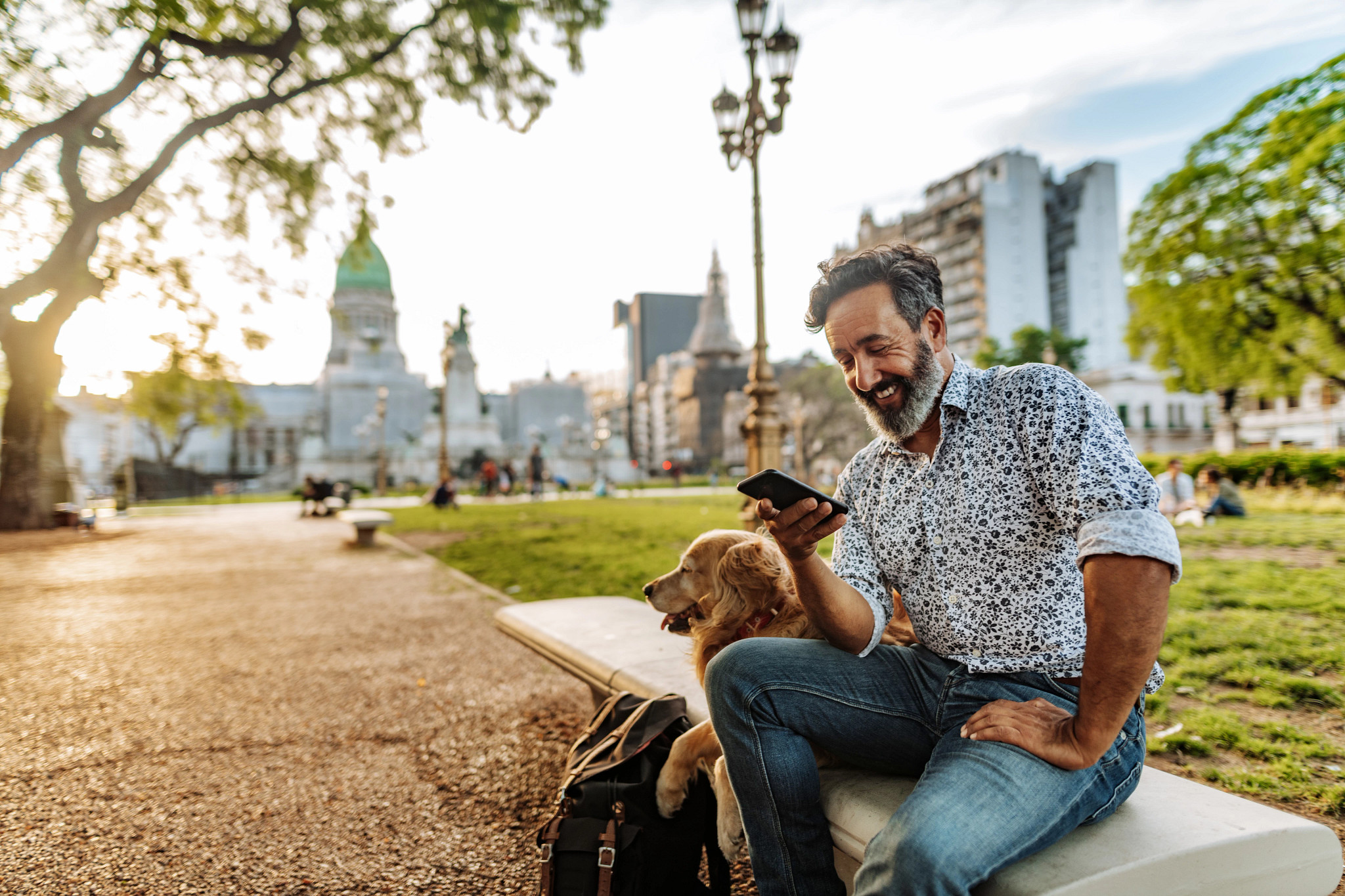 A man looks at his phone while sitting on a park bench.