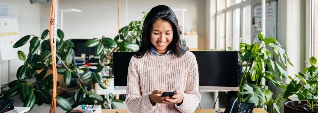Personne debout dans un bureau souriant en regardant son téléphone