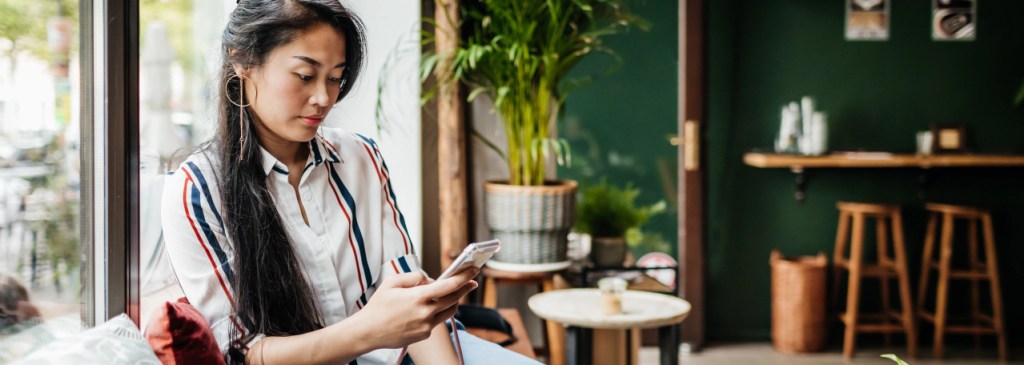 Seseorang duduk di kafe sambil membaca di telepon