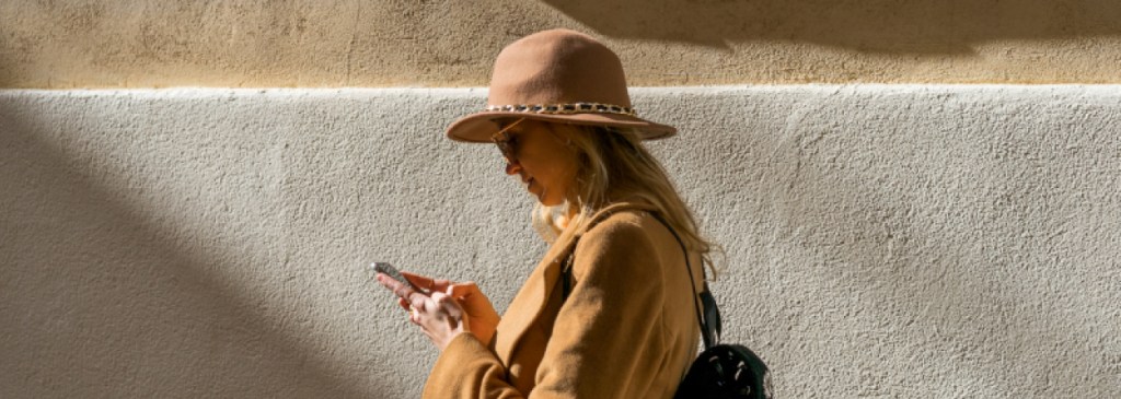 Orang berjalan di depan dinding berwarna beige sambil membaca pesan WhatsApp di telepon