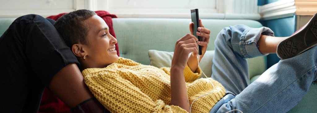 Seseorang bersandar di kaki seseorang di sofa sambil membaca pesan WhatsApp bisnis