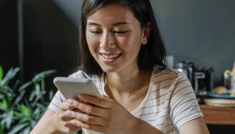 Seseorang duduk di depan meja makan sambil membaca pesan layanan keuangan melalui WhatsApp