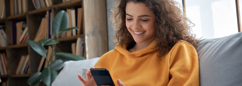 Seseorang duduk di atas sofa abu-abu mengenakan sweter kuning, melakukan pembelian dari pesan bisnis WhatsApp
