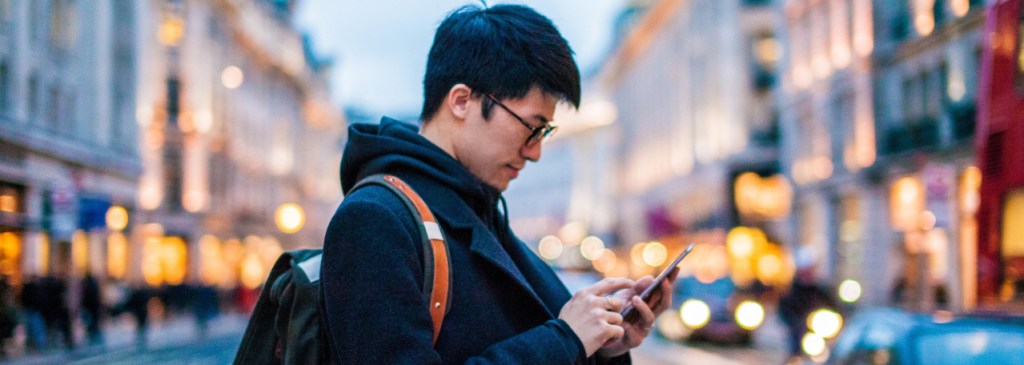 Persona de pie en medio de una calle iluminada mientras lee un mensaje de WhatsApp en el teléfono