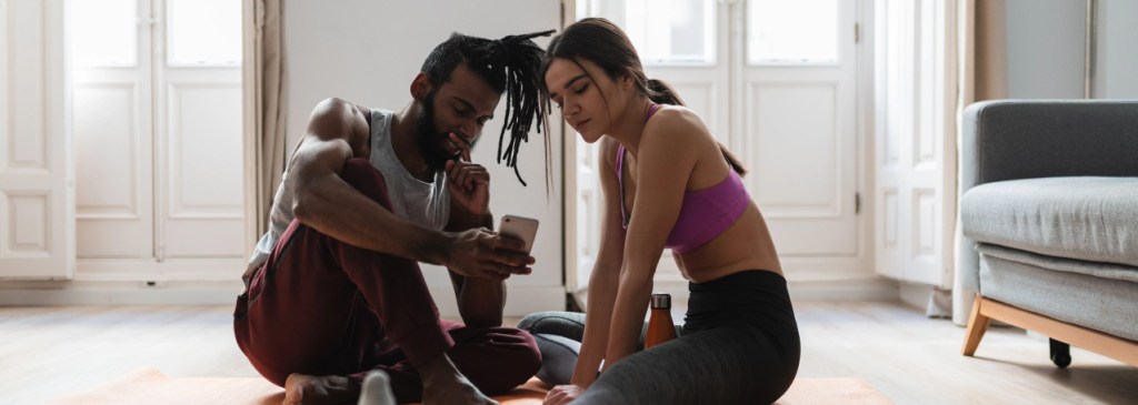 Dua orang duduk di lantai setelah kelas yoga membaca notifikasi WhatsApp