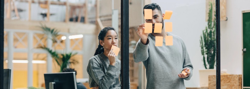 Deux collègues faisant un brainstorming à l’aide de notes autocollantes sur la fenêtre d’un bureau