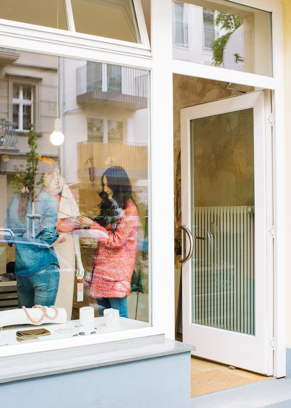 Une femme en manteau rouge regardant la vitrine d’un magasin. Son reflet apparaît sur la vitre