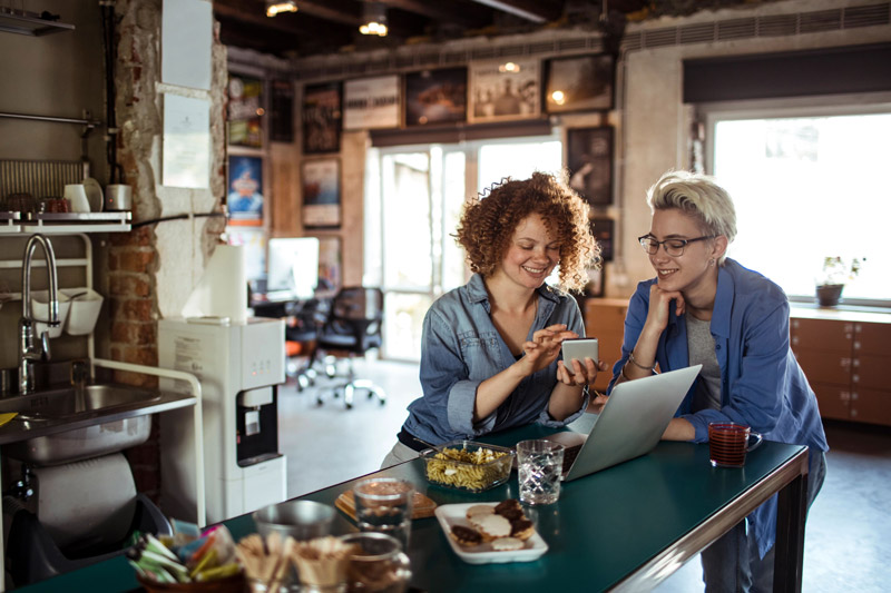 Two people at an office kitchen table, looking at a phone