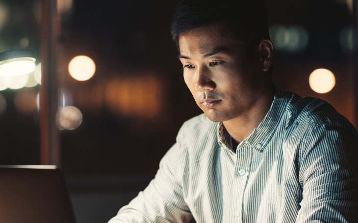 Personne assise à un bureau travaillant sur un ordinateur portable le soir